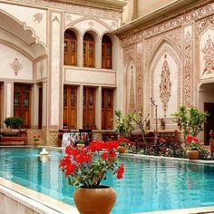 an indoor swimming pool with red flowers in the foreground and ornately decorated walls