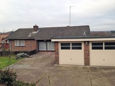 two garages in front of a brick house with grass and bushes around the driveway