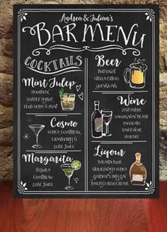 a chalkboard sign with drinks on it next to a wooden table and stone wall