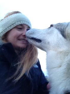 a woman is kissing her husky dog on the nose while wearing a beanie hat