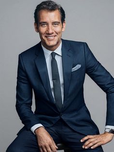 a man in a suit and tie sitting on top of a chair smiling at the camera