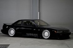 a black nissan car parked in front of a garage door with roller doors behind it