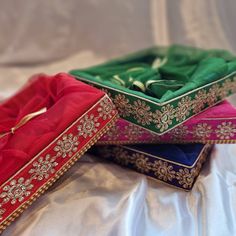 three different colored boxes sitting on top of a white cloth covered tablecloth with gold trimmings