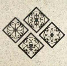 three square metal wall art pieces on a white marble surface with black ironwork designs