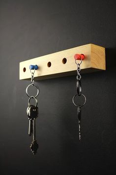 two keys are hanging on a wooden key holder attached to a black wall with hooks