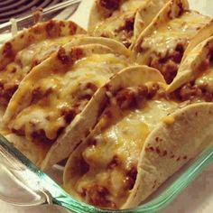 several tacos sitting in a glass dish on top of a blue plate with cheese