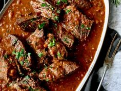 beef stew in a white dish with spoons and garnish on the side