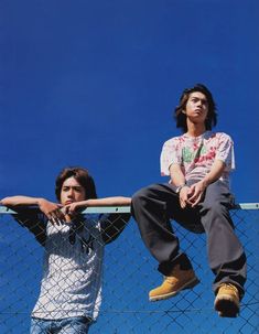 two young men sitting on top of a fence with their arms crossed and looking up at the sky