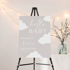 a baby shower sign sitting on top of a easel next to a vase filled with flowers