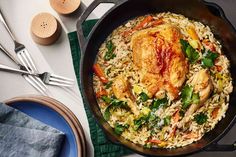 a chicken and rice dish in a skillet with utensils on the side