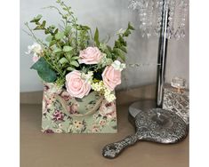 a small bag with flowers and greenery in it sitting on a table next to a mirror