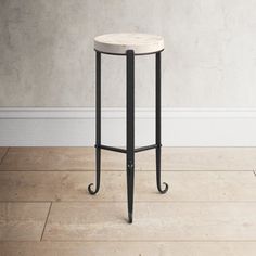 a white marble top side table with black metal legs on a wooden floor in front of a gray wall