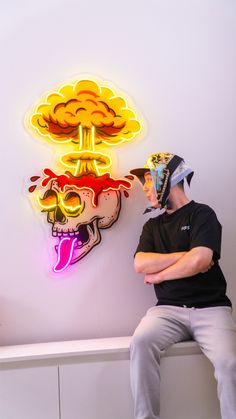 a man sitting in front of a neon sign with a skull on it's head