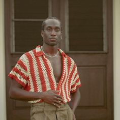 a man standing in front of a door wearing a red and white striped shirt with his hands on his hips