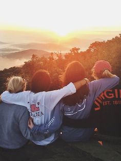 three people sitting on top of a mountain looking at the sunset