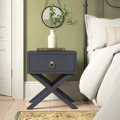 a nightstand with a plant on it next to a bed in a green walled room