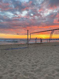 two people playing volleyball on the beach at sunset