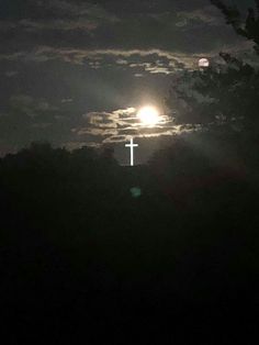 the moon is shining brightly in the night sky over trees and a cross on a hill