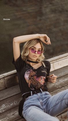 a woman sitting on top of a wooden bench next to a lake and wearing sunglasses