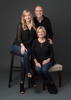 two women and a man are sitting on a stool together, posing for the camera