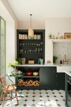 a kitchen with black cabinets and white tile flooring, an open shelving unit filled with books