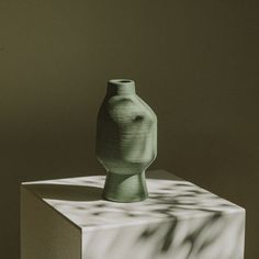 a green vase sitting on top of a block of white paper next to a shadow