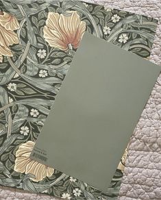 a book laying on top of a bed next to a flowered wallpaper pattern