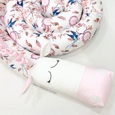 a pink and blue flowered neck pillow next to a rolled up tube on a white surface