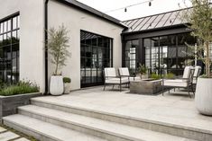 an outdoor patio with chairs, tables and potted plants in front of the house