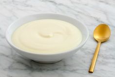 a bowl of yogurt next to a golden spoon on a marble countertop