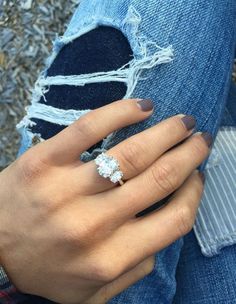 a woman wearing an engagement ring on her left hand, sitting in ripped jeans and looking at the camera