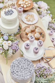 a table topped with cakes and cupcakes on top of plates next to flowers