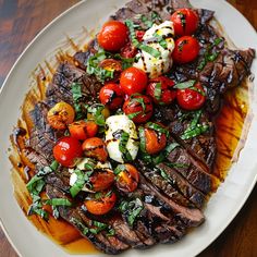 steak with cherry tomatoes and mozzarella sauce on a white plate sitting on a wooden table