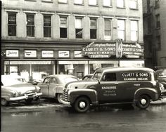 an old black and white photo of cars parked in front of a building on a city street