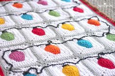 a white crocheted blanket with multicolored balls on the edges and a red border