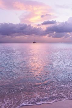 an ocean view with waves coming in to shore and a sailboat on the horizon