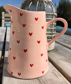 a pink pitcher sitting on top of a wooden table next to a vase with hearts painted on it