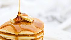 a stack of pancakes topped with syrup and banana slices, on a white tablecloth