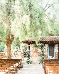 an outdoor ceremony setup with wooden chairs and greenery on the outside, in front of a stone building