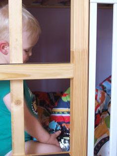 a young boy playing with toys in a wooden bunk bed frame, while looking through the window