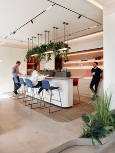 three people are sitting at a bar in the middle of a room with plants on it