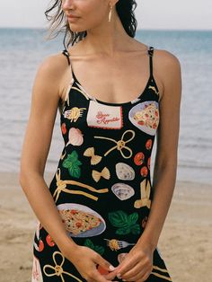 a woman standing on the beach wearing a black dress with colorful pictures and words all over it