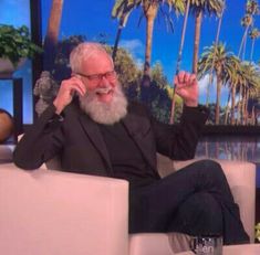 an older man sitting in a chair talking on a cell phone and holding his hand up to his ear