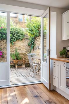 an open patio door in a kitchen with wooden flooring and white cabinetry on either side