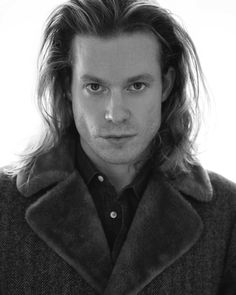 a black and white photo of a man with long hair wearing a peal coat