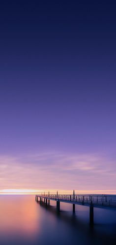 a long pier sitting on top of a body of water under a purple and blue sky