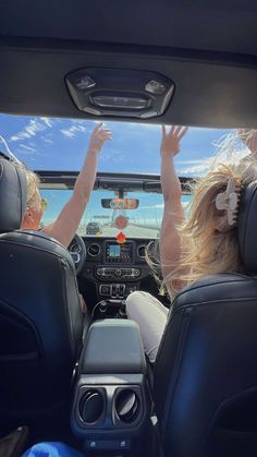 two people sitting in the back seat of a car with their hands up to the sky