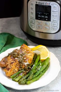 a plate with chicken, asparagus and lemon on it next to an instant pot