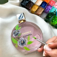 a person holding a pen in front of a chanel bottle with flowers painted on it