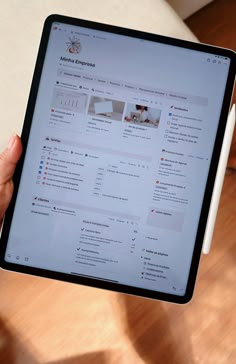 a person holding up an ipad with the homepage displayed on it, in front of a wooden table